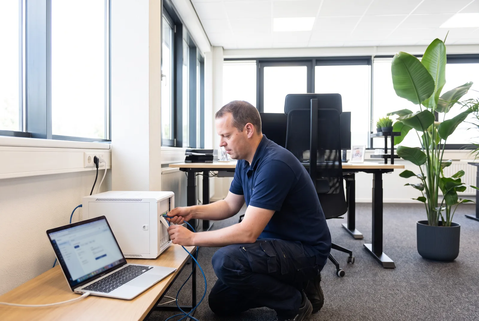 Jordy van Boutio sluit een netwerkkast aan op kantoor, met een laptop ernaast